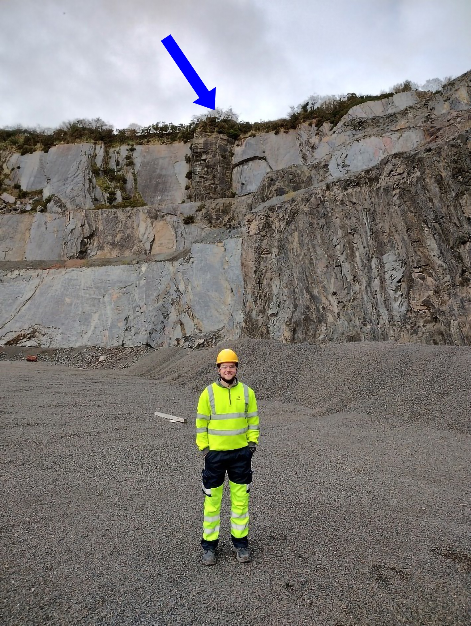 Scientist stands in a quarry with dolerite dyes in rock face behind