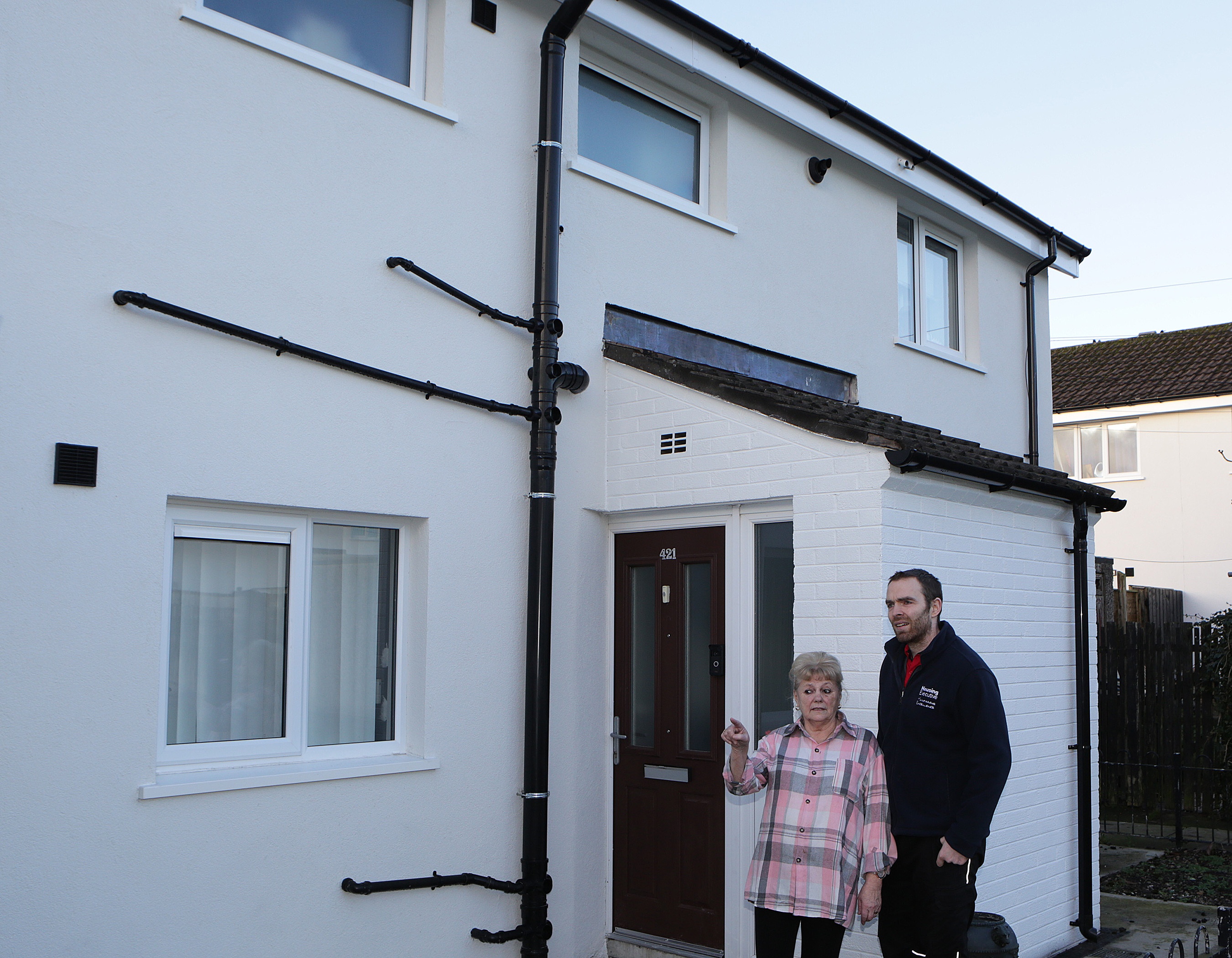 Housing Executive contractor and householder pose outside a neat, white house.